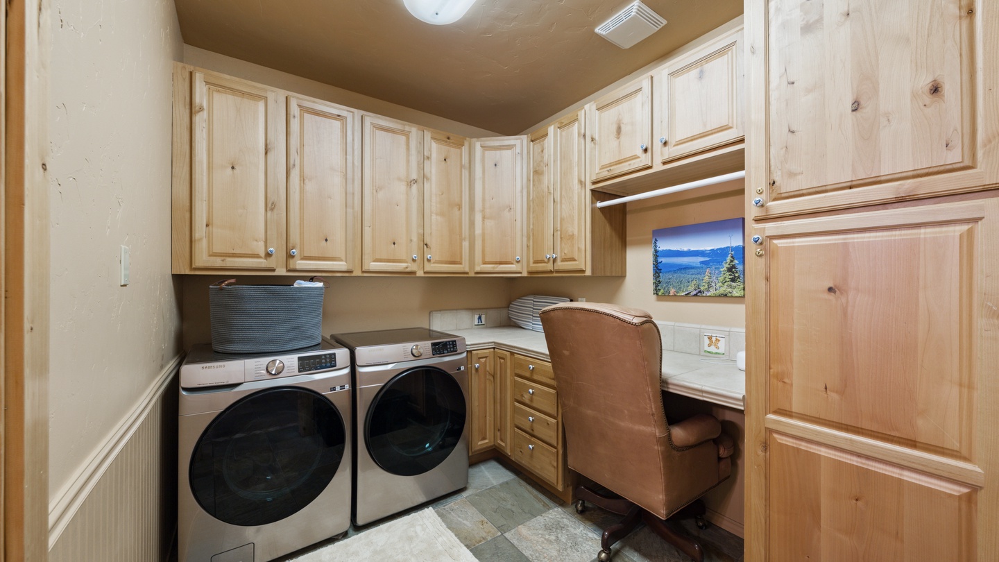 Your laundry room doubles as a functional workspace, with beautiful natural wood cabinetry, a handy desk area, and modern front-loading washer and dryer making chores a breeze.