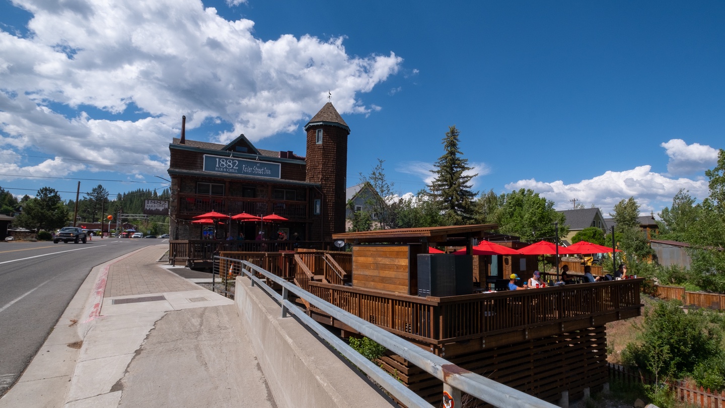Historic 1882 restaurant with charming red umbrellas and outdoor dining deck surrounded by mountain scenery and tall pines.