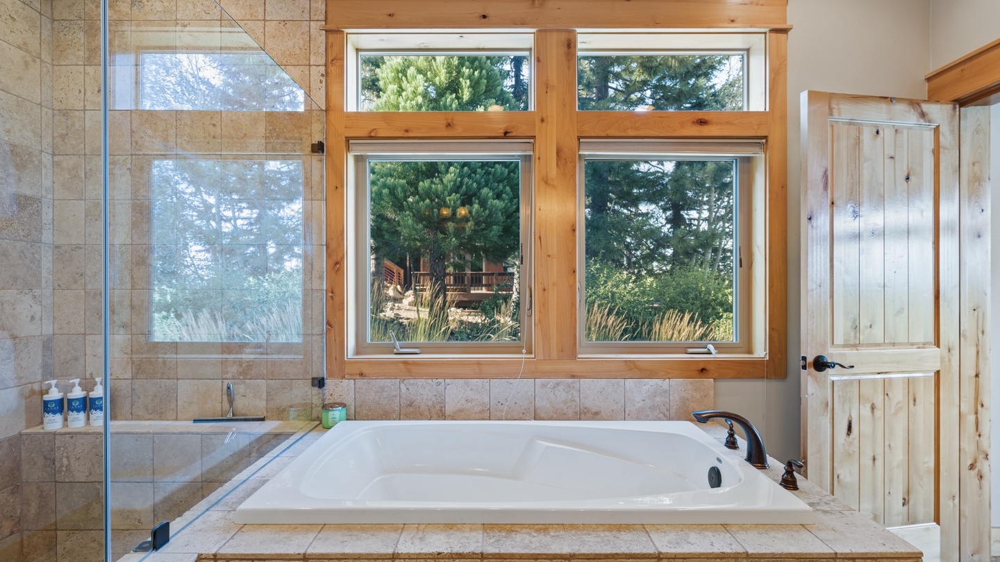 Unwind in your private bathroom sanctuary, where a soaking tub sits beneath wooden-framed windows offering tranquil views of surrounding greenery and natural beauty.