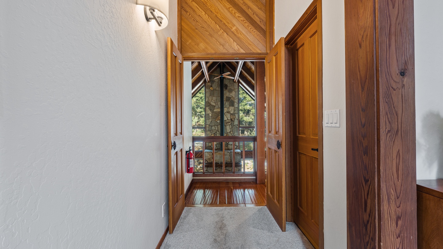 Step into a serene entryway where rich wood tones and soaring vaulted ceilings welcome you, with natural light streaming through windows that frame peaceful wooded views beyond.