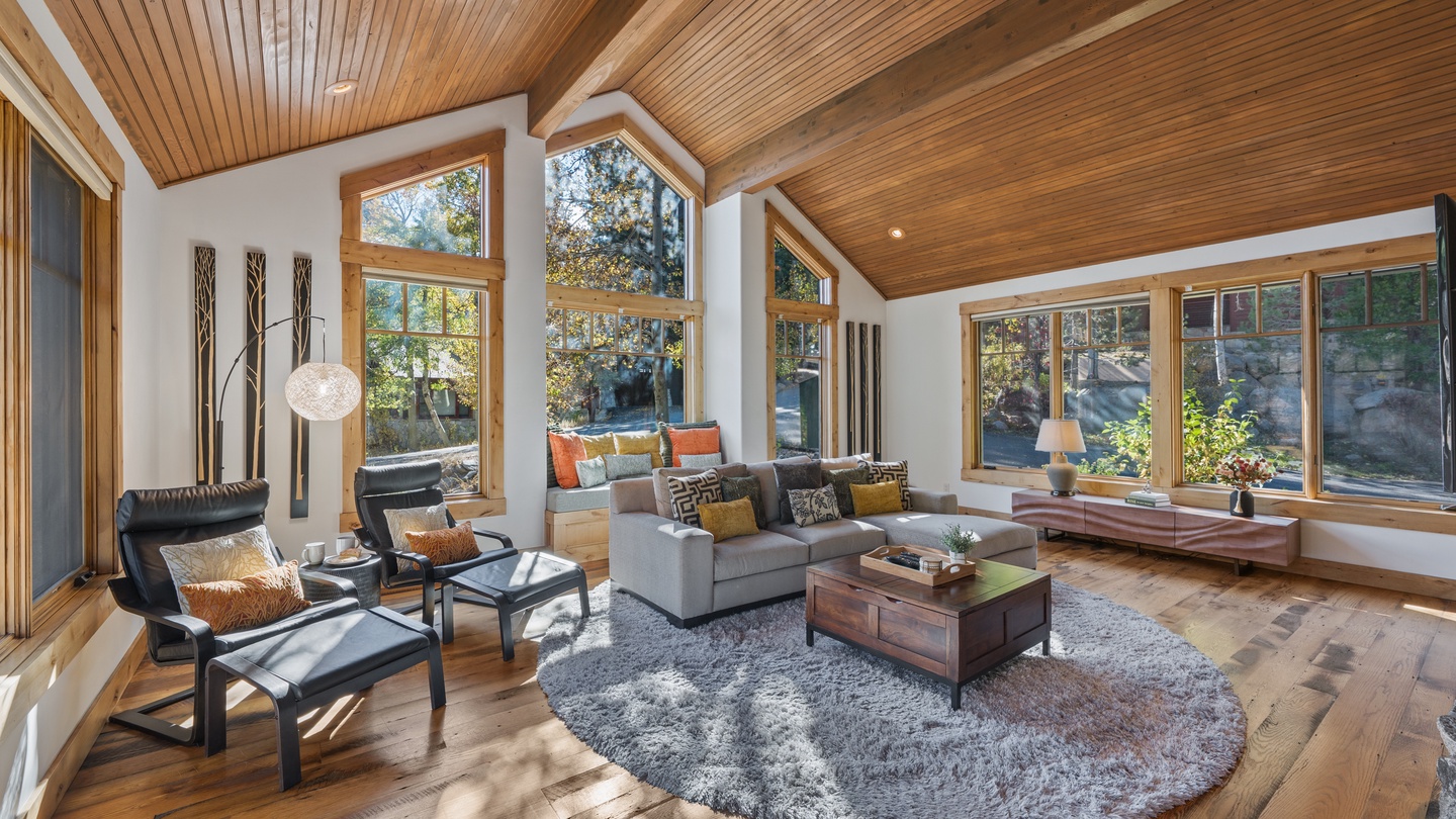 Sink into plush seating beneath soaring wood ceilings while natural light pours through floor-to-ceiling windows, framing tranquil forest views that bring the outdoors in.