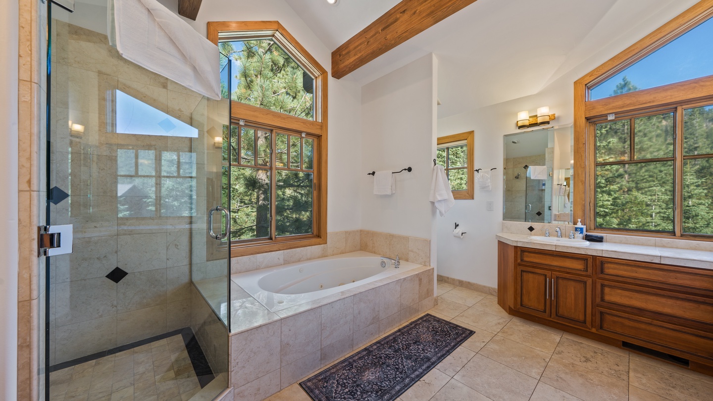 Soak in your spacious tub surrounded by natural light and forest views, or refresh under a rain-style shower in this elegant bathroom. Vaulted ceilings and warm wood beams create a serene mountain retreat feel.