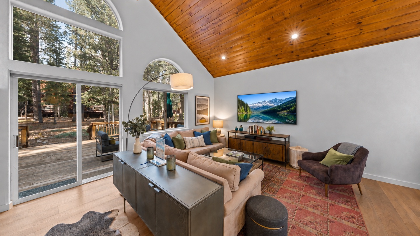 Unwind beneath soaring wood-paneled ceilings in this airy living room, where tall windows frame views of towering pines and your private deck awaits just beyond the glass doors.