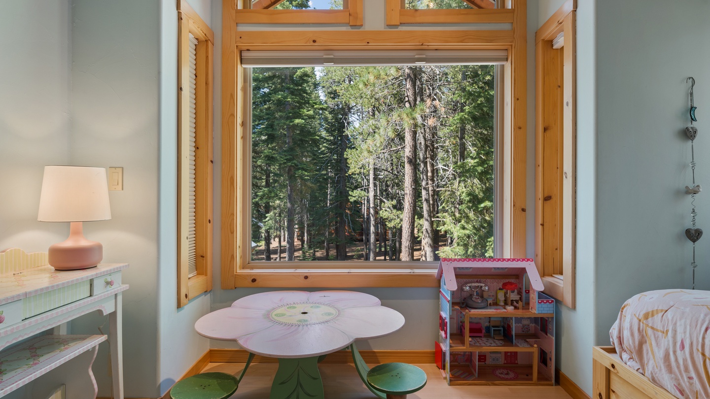 A charming child's hideaway with a whimsical flower-shaped table beneath cathedral windows overlooking towering pines. Soft natural light creates the perfect spot for creative play and peaceful moments.