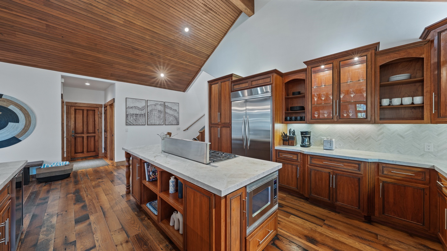 Step into your gourmet kitchen featuring rich wood cabinetry, marble countertops, and vaulted ceilings that create an airy, elegant space perfect for cooking and gathering.
