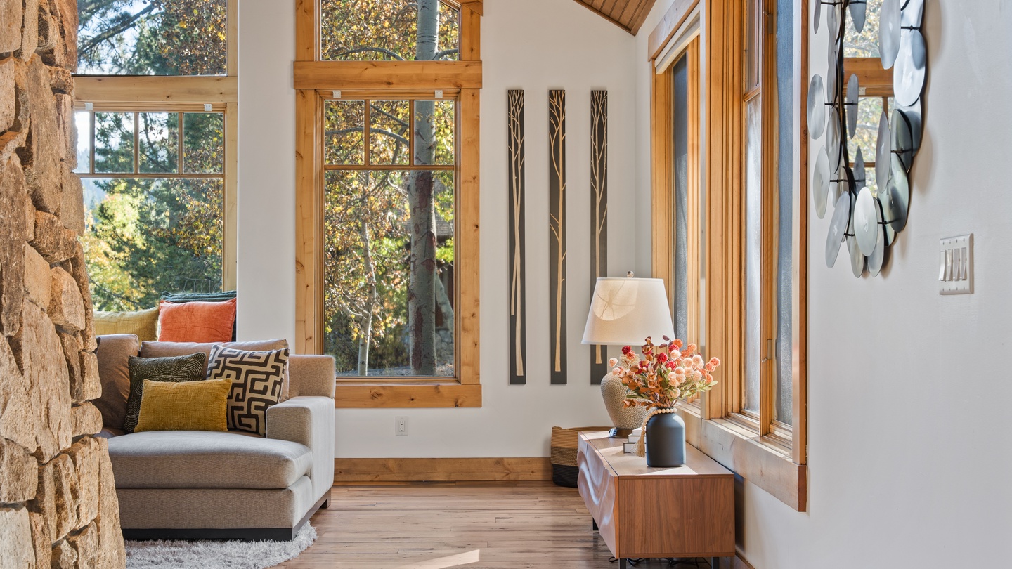 Settle into this sunlit living space where natural wood and stone create a warm mountain retreat. Large windows frame forest views, inviting you to unwind and reconnect with nature.