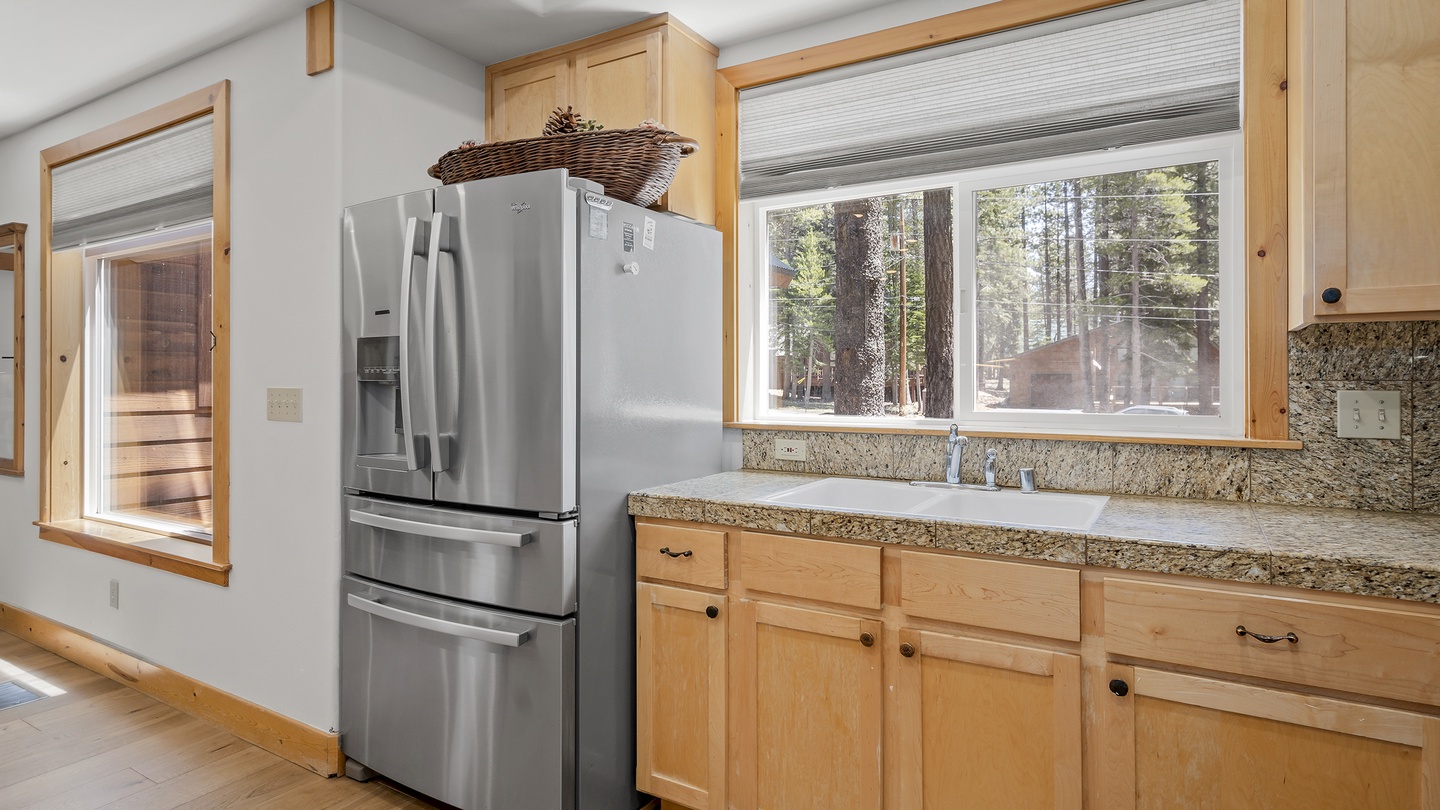 A bright kitchen space featuring granite counters, blonde wood cabinetry, and views of towering pines—perfect for cooking meals together during your forest getaway.