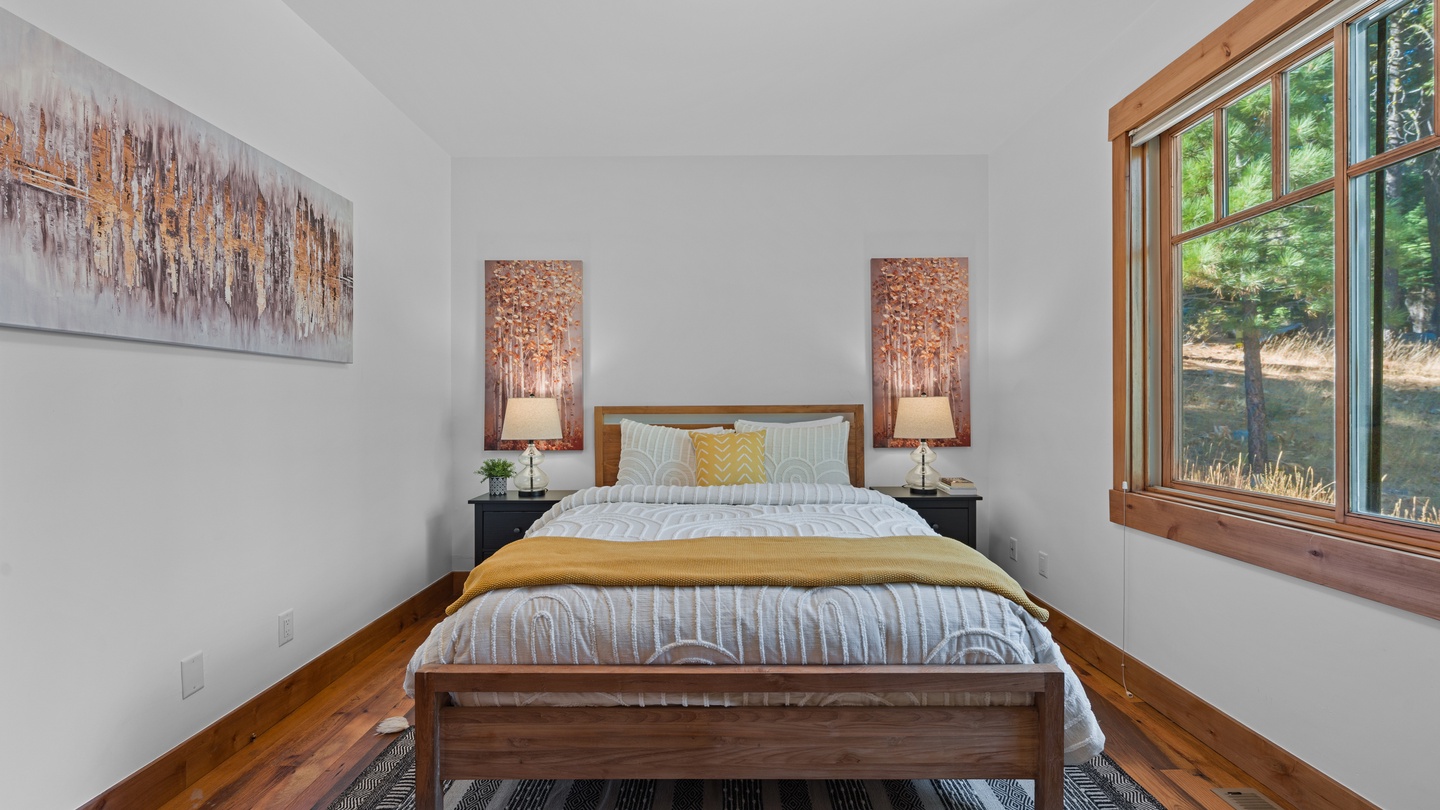 Wake up to warm wood tones and natural light streaming through your bedroom's generous windows, where peaceful forest views greet you each morning from the comfort of your cozy bed.