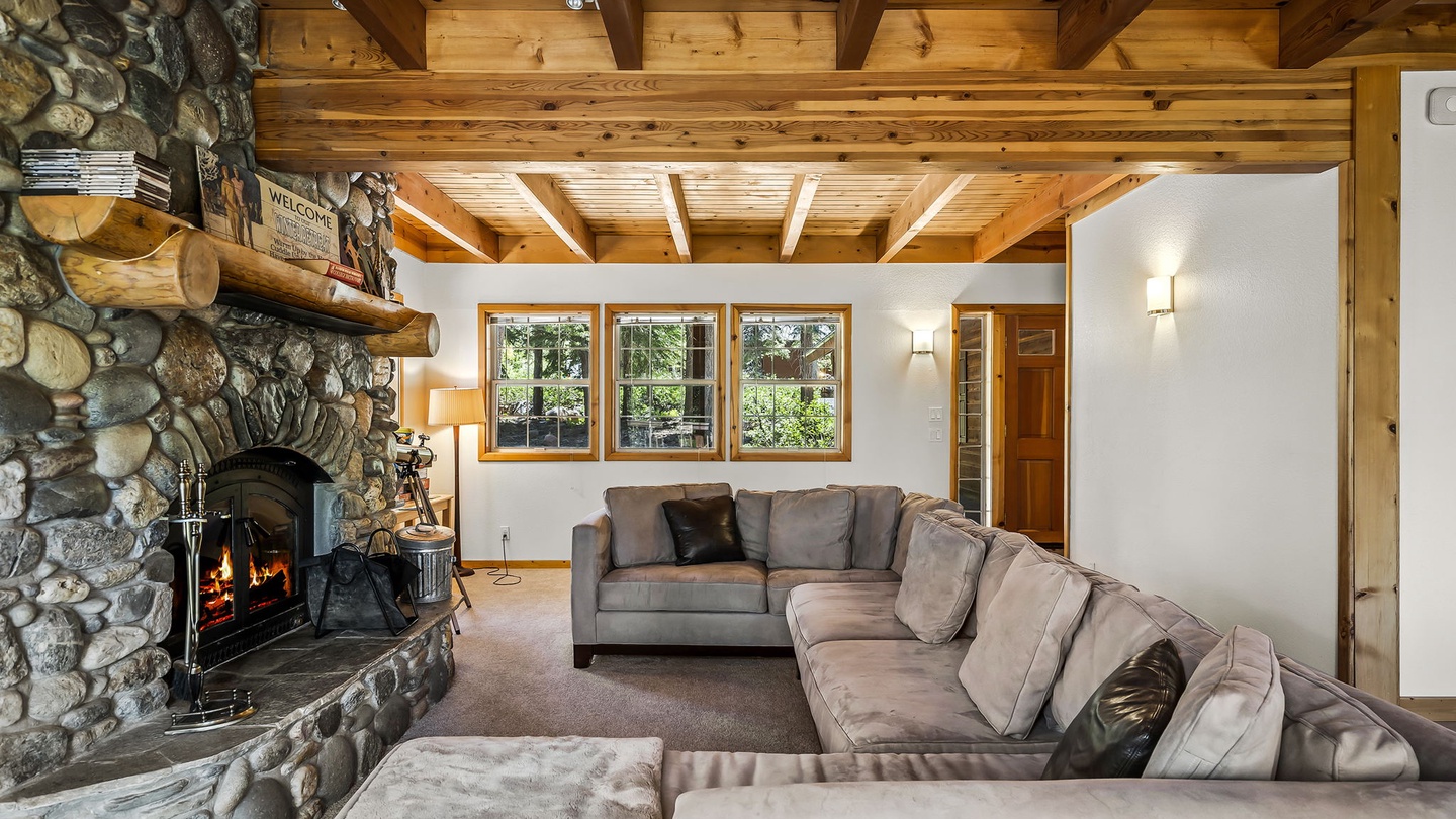 Gather around the crackling stone fireplace and sink into plush seating beneath soaring wood-beamed ceilings. Natural light pours through the windows, creating your perfect mountain retreat.