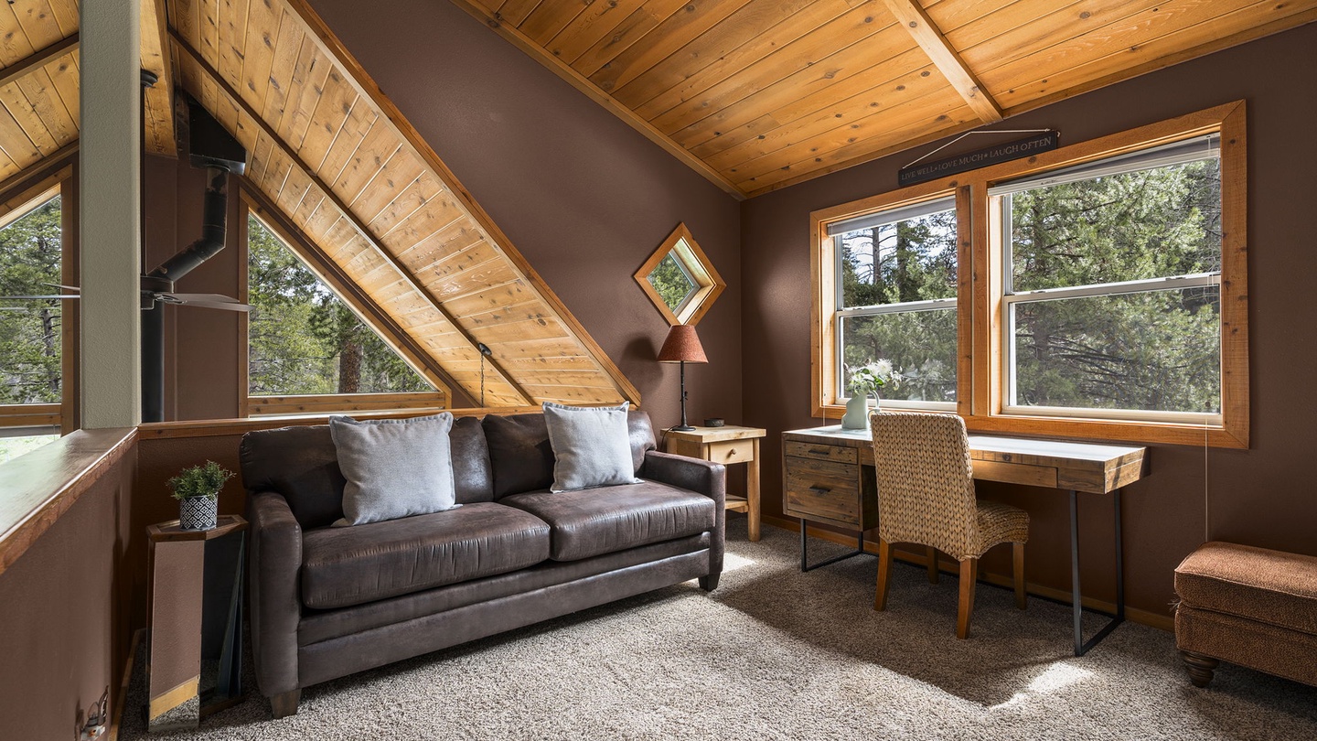 Unwind in your cozy loft lounge with leather seating, workspace, and forest views through cathedral windows.