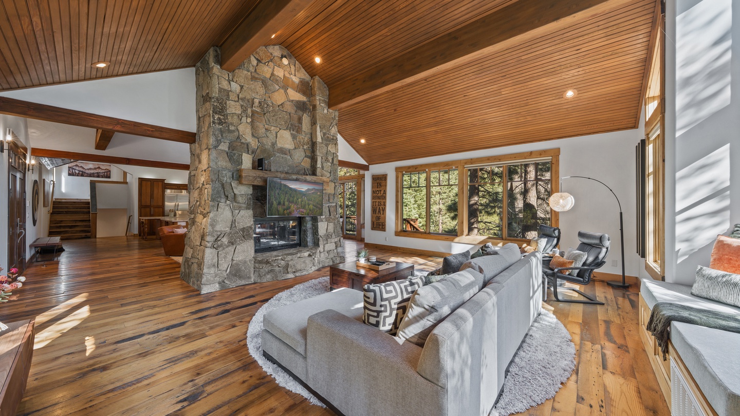 Unwind in your spacious living room where sunlight streams through expansive windows and a stunning stone fireplace anchors the warm, wood-lined space—your perfect mountain retreat awaits.