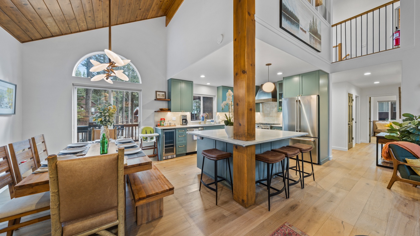 Step into an inviting open-concept space where your vacation unfolds under soaring wood-beamed ceilings. Your culinary adventures begin at the spacious island, while dining awaits beside windows framing peaceful forest views.