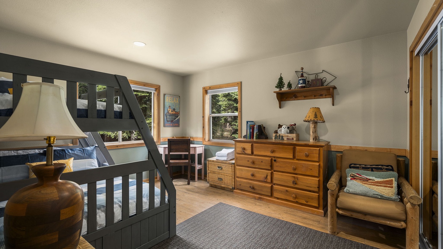 Your cozy bedroom features rustic wood furniture, charming bunk beds, and peaceful garden views through bright windows.