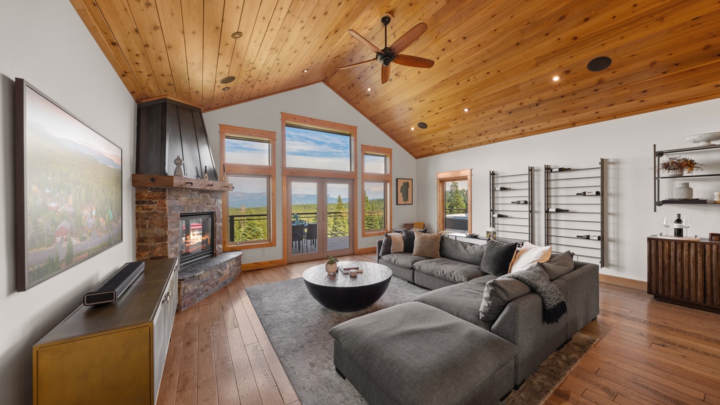 Unwind in your spacious living room featuring a cozy fireplace, vaulted wood ceiling, and floor-to-ceiling windows framing spectacular mountain views that invite the outdoors in.
