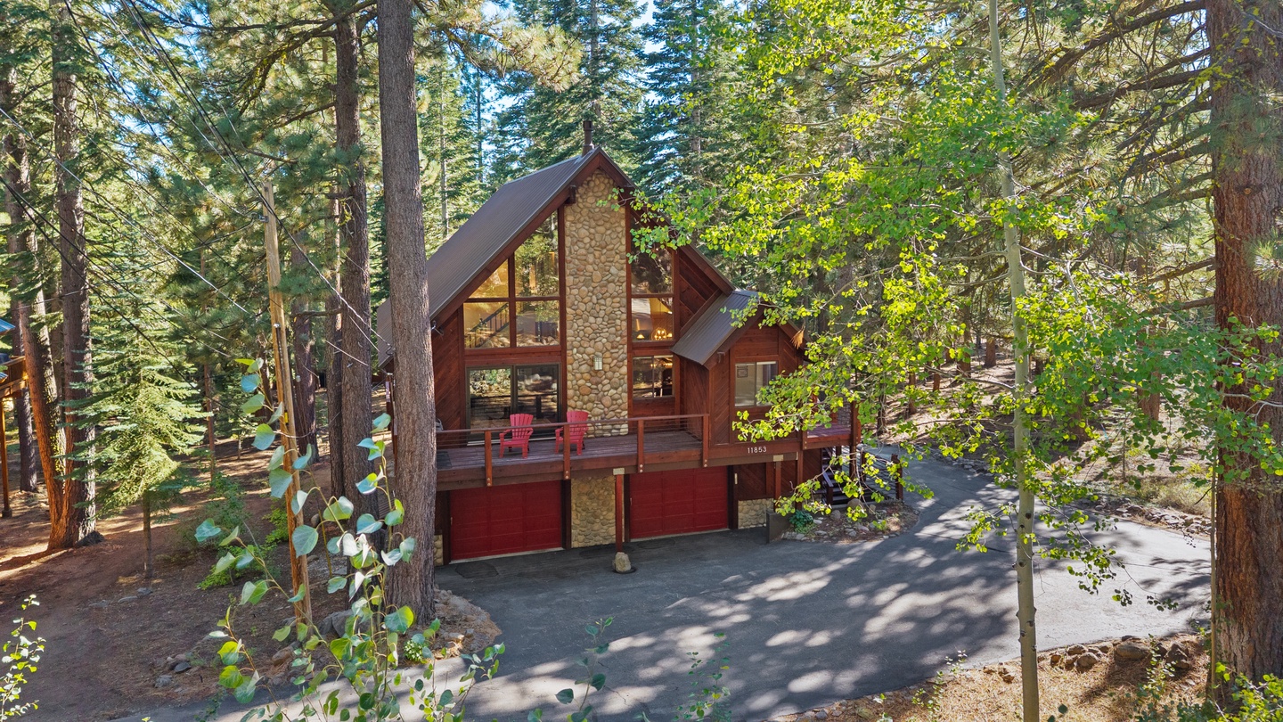 A striking A-frame cabin nestled in a peaceful forest setting, featuring warm wood tones, expansive windows, and a spacious deck surrounded by towering pines and aspen trees.
