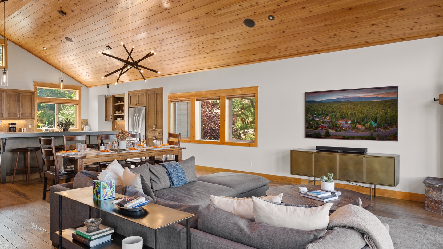 Settle into plush seating beneath soaring wood ceilings where warm natural light streams through picture windows, inviting you to unwind in this beautifully appointed open-concept living and dining space.