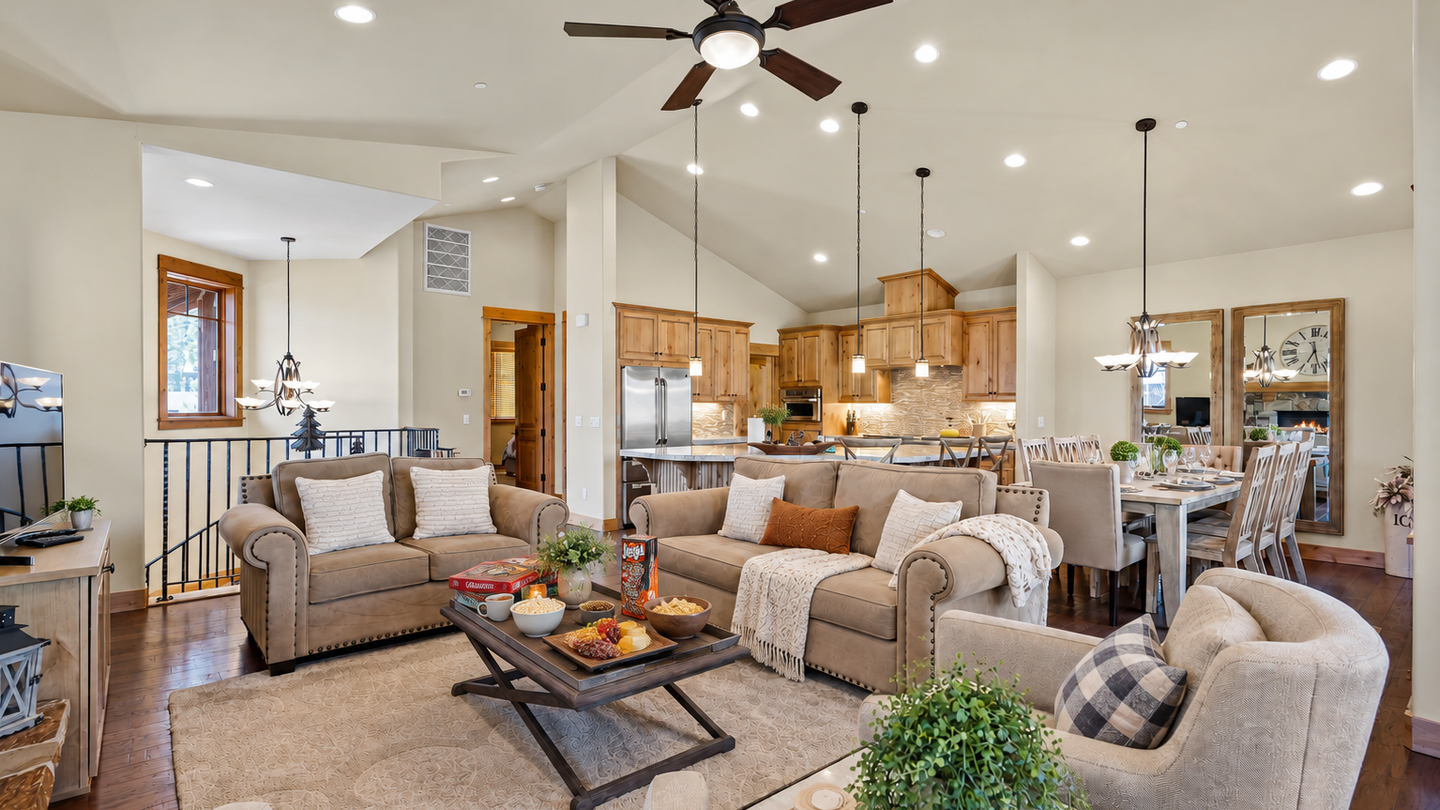 Spacious open-concept retreat with vaulted ceilings and warm wood tones. Plush living room seating flows into a bright kitchen and dining area, perfect for family gatherings.