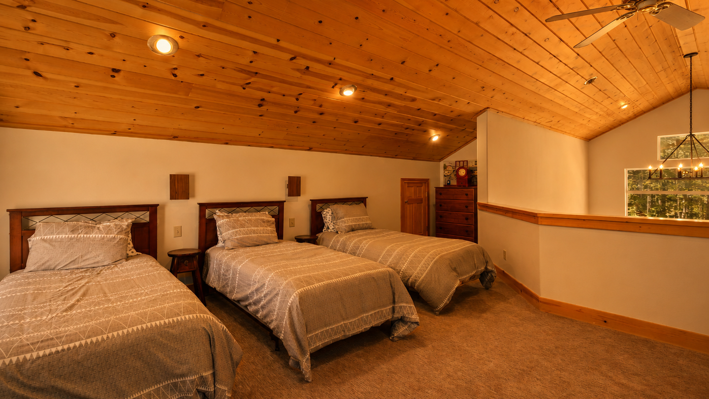 Relax in your spacious loft bedroom with three comfortable beds, warm wooden ceilings, and soft lighting creating a cozy mountain retreat atmosphere for your group.