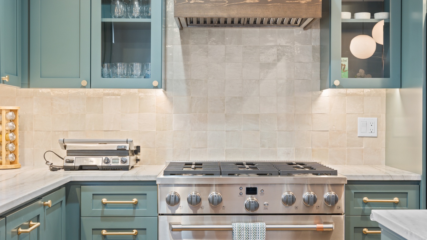 This well-appointed kitchen features a professional-grade gas range, elegant tile backsplash, and custom cabinetry in calming teal tones—your perfect space for preparing meals during your stay.