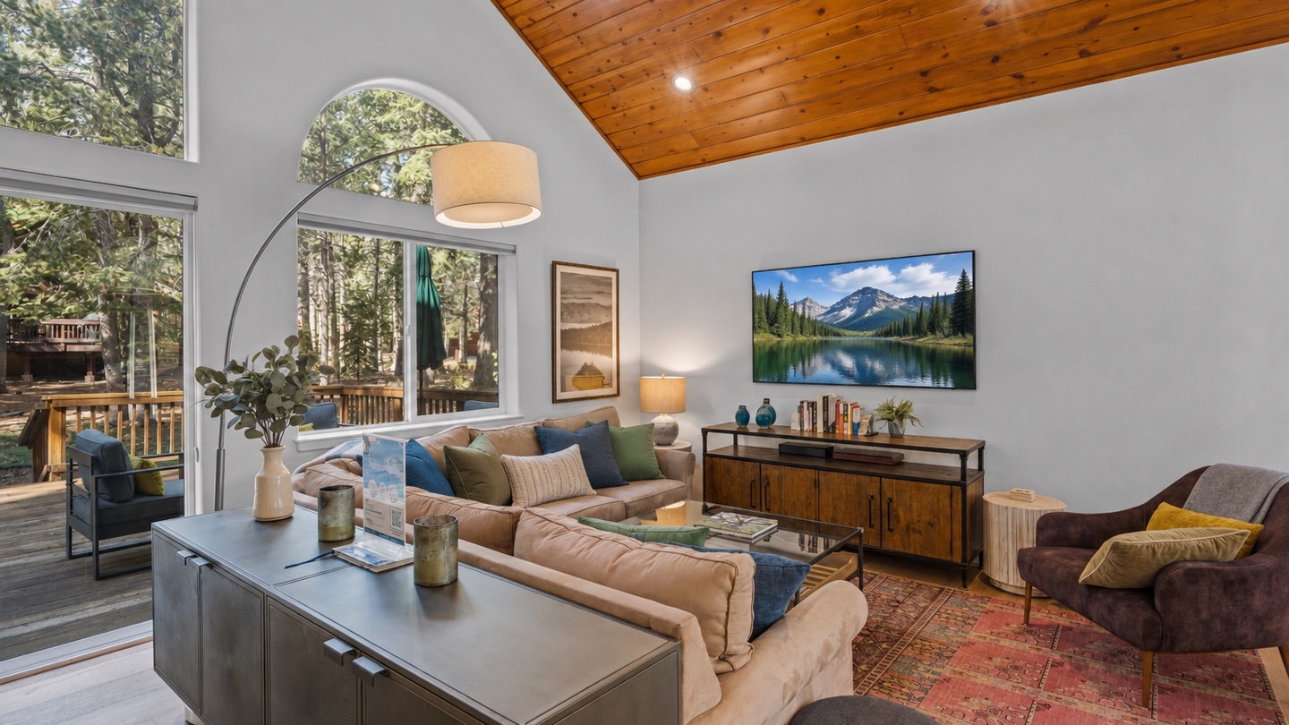 Settle into this bright living room where soaring ceilings meet warm wood tones and forest views through expansive windows invite you to unwind in comfort and style.
