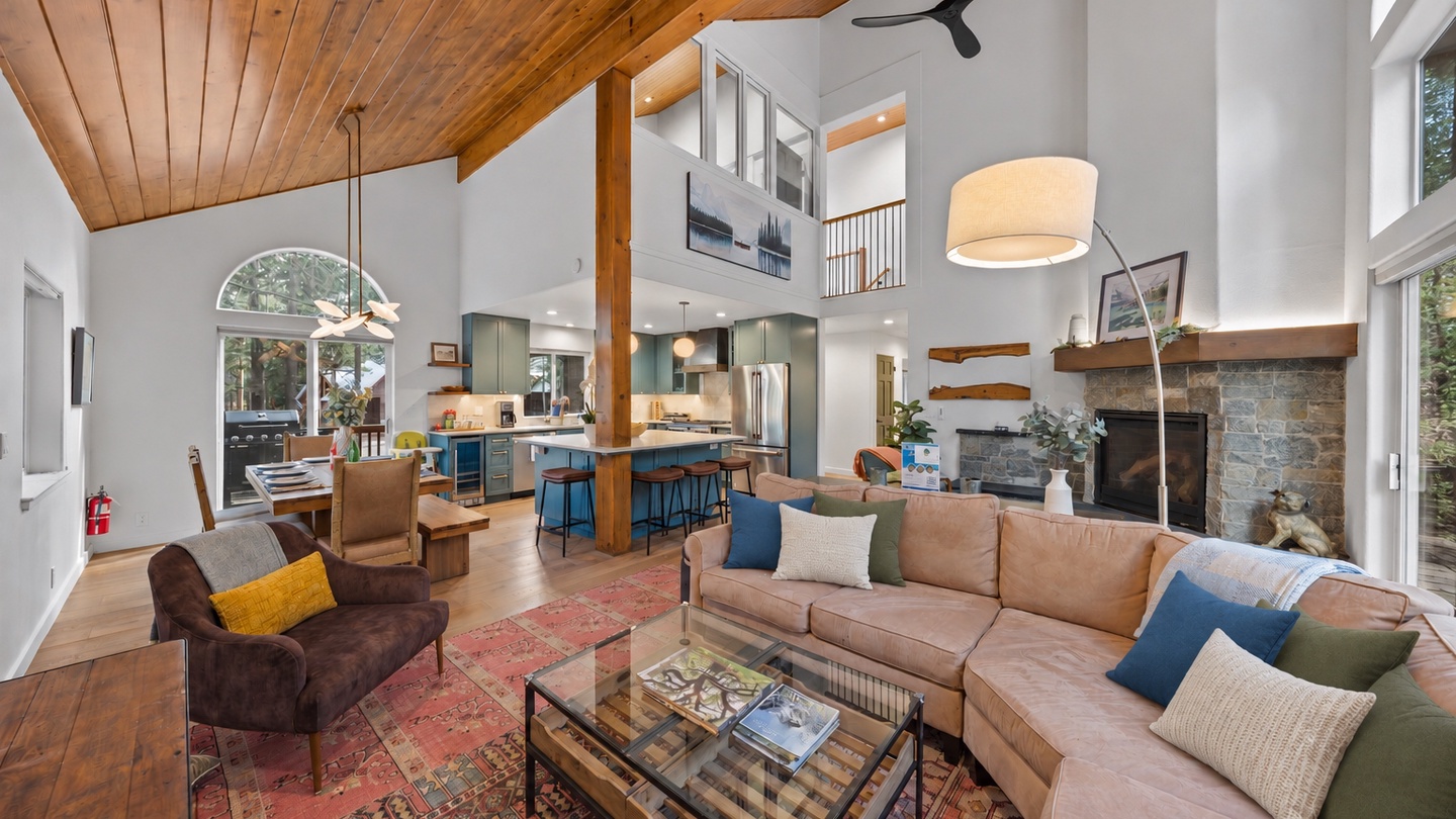 Spacious open-plan living area with soaring wood-beam ceilings, natural light, stone fireplace, and seamless flow to the kitchen—the perfect retreat.
