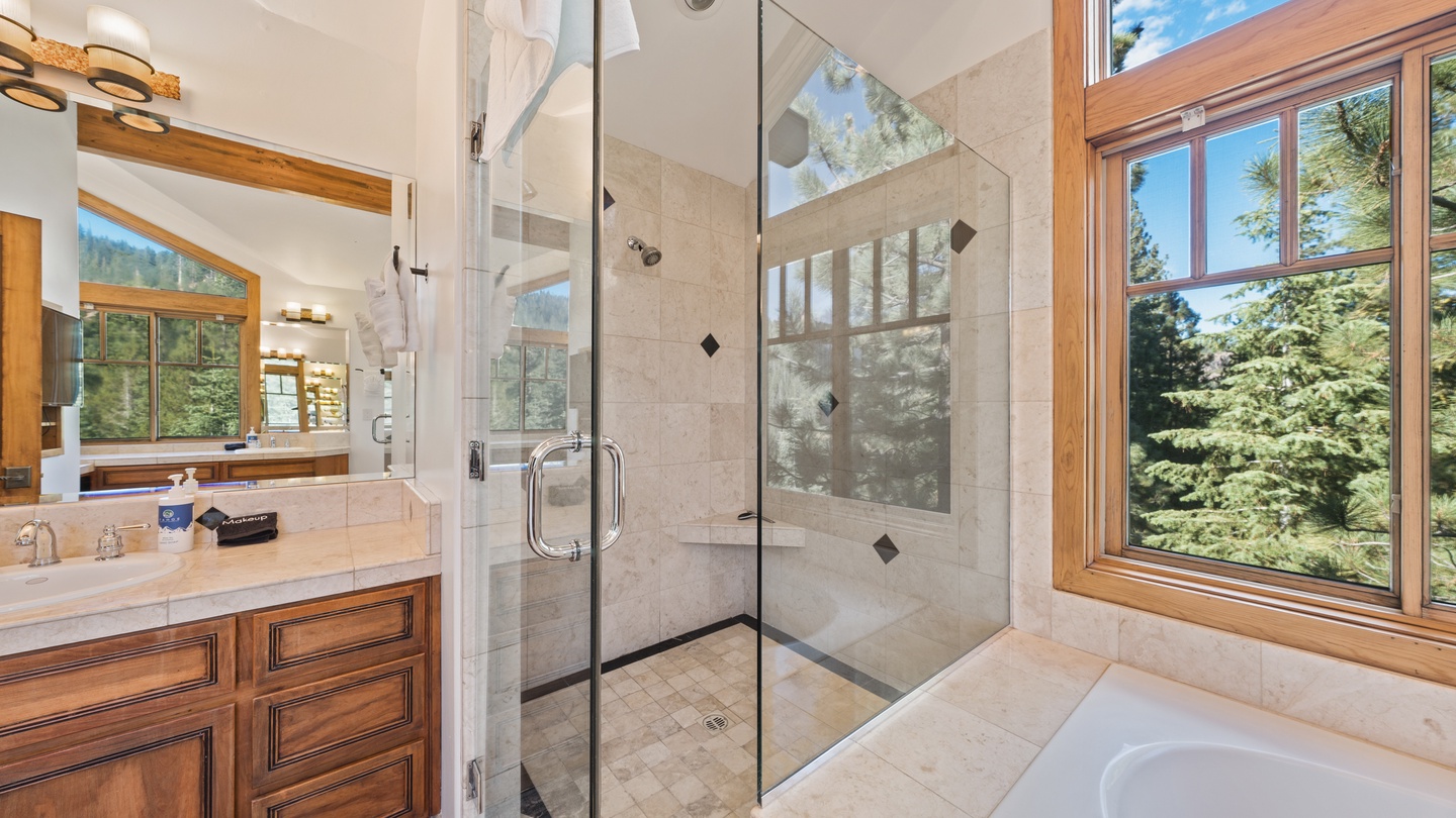 Sunlight pours into your spacious bathroom, where forest views frame the glass shower and soaking tub. A peaceful retreat with natural beauty right outside your window.