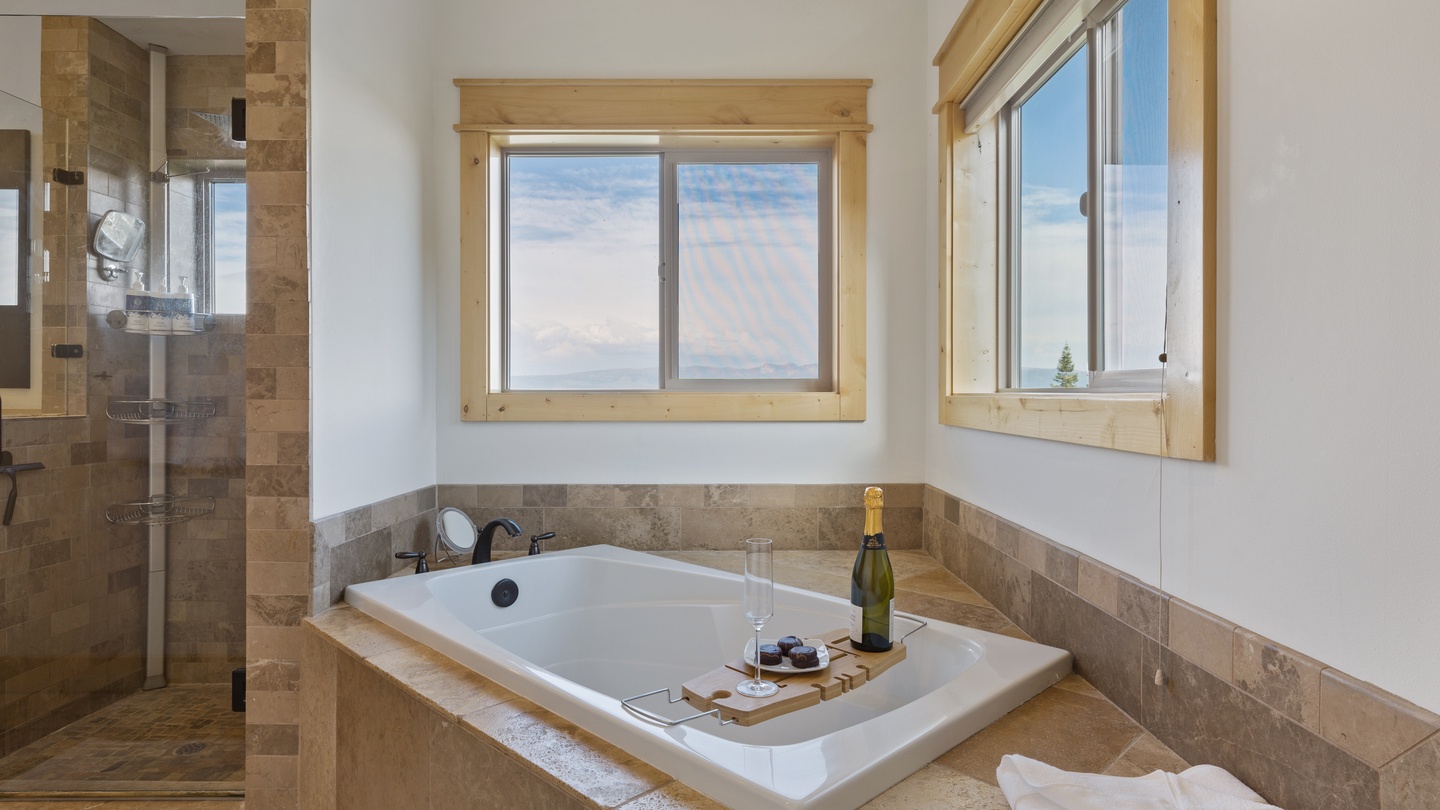 Indulge in a luxurious soak with champagne at hand while you gaze out at stunning mountain views through large windows. The spa-like bathroom features elegant stone tile and a spacious glass-enclosed shower.