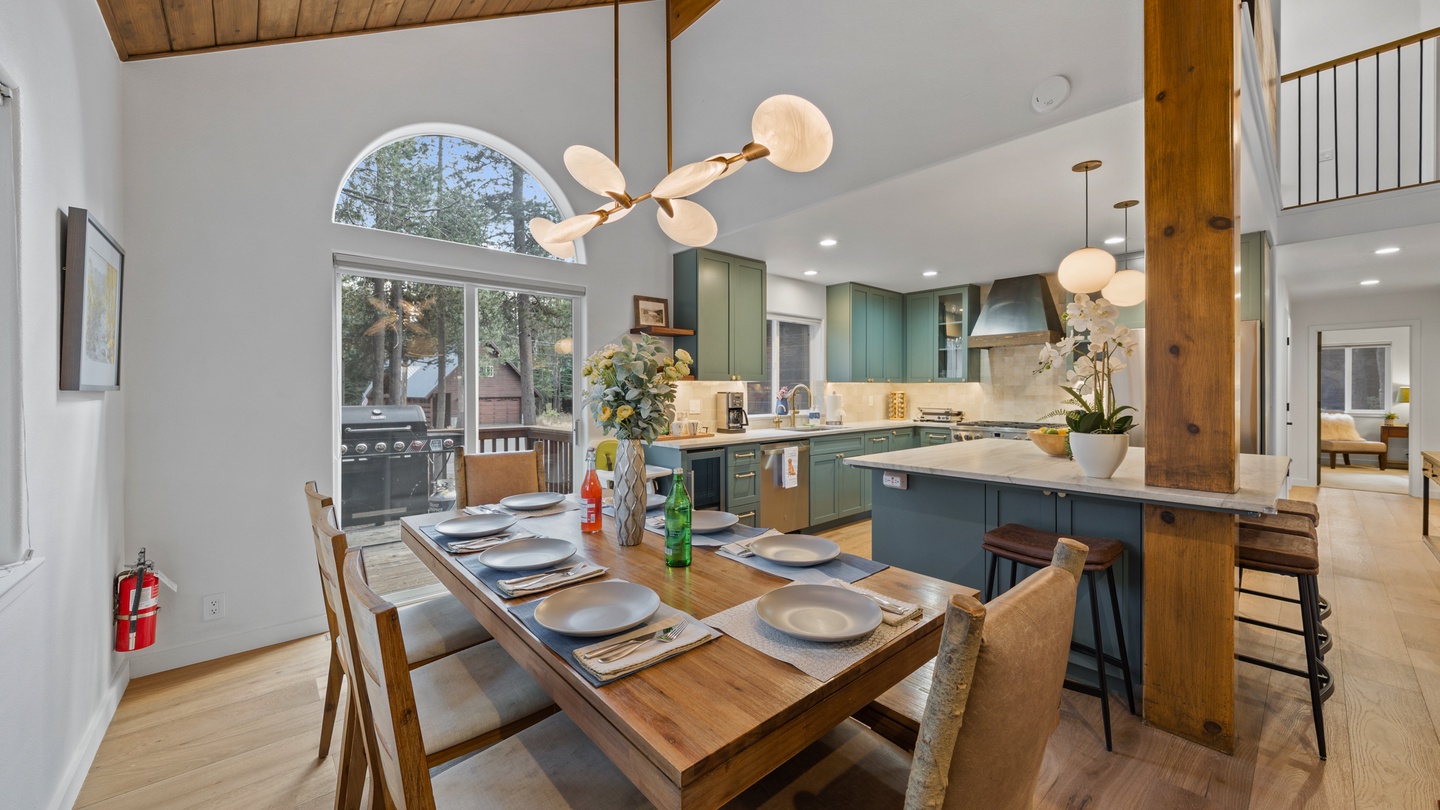 Your open-concept dining and kitchen space combines natural wood warmth with modern design. Cook together in the spacious teal-green kitchen, then gather at the table beneath soaring ceilings and natural light.