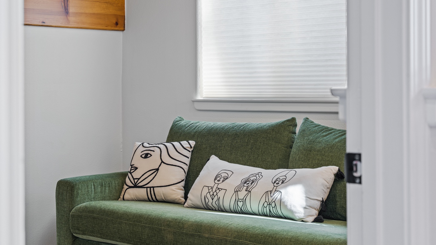 Sink into this lush green sofa with playful pillows and let natural light fill your cozy retreat—perfect for curling up with a book or simply unwinding after exploring the area.