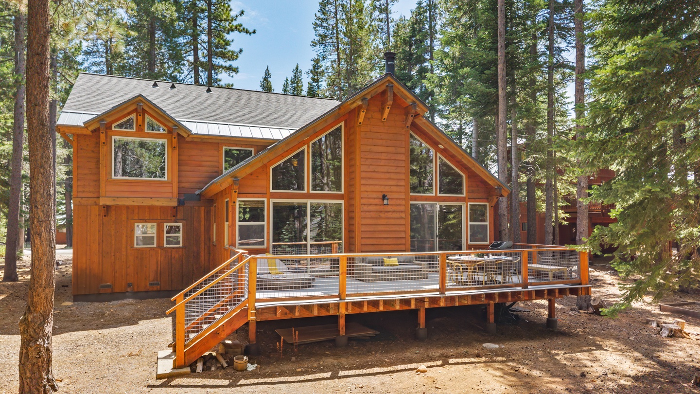 A beautiful mountain retreat nestled among towering pines, featuring natural wood siding, expansive windows, and a spacious wraparound deck perfect for enjoying the peaceful forest surroundings.