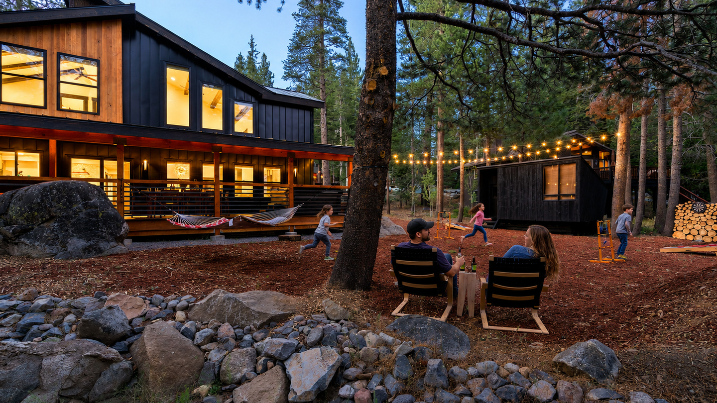 A modern mountain retreat nestled among towering pines, where families gather under string lights on a spacious wooded lot with a separate guest cabin and hammock deck.