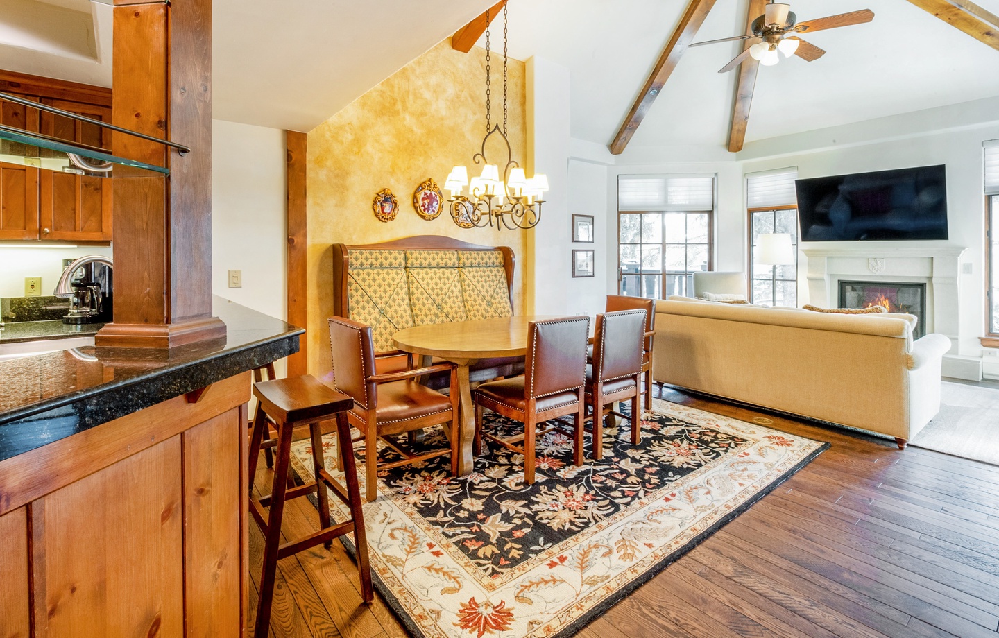 Gather around the dining table for meals and conversation, with the warmth of exposed beams overhead and a cozy fireplace glowing nearby. The open layout connects kitchen, dining, and living spaces effortlessly.