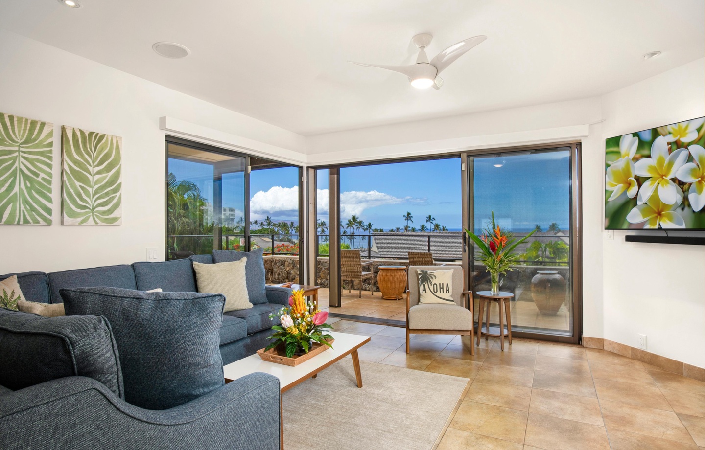 Settle into your bright living space where tropical breezes drift through open lanai doors. Sink into the plush sofa, admire the vibrant island florals, and soak in the stunning ocean and palm tree views just beyond your private balcony.