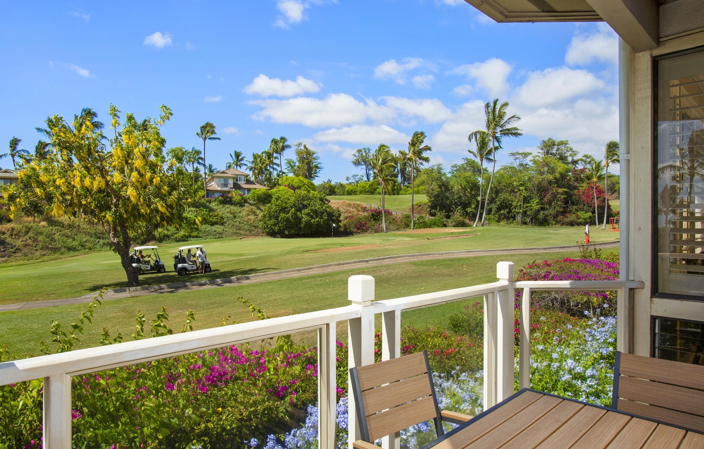 Covered lanai overlooking manicured golf course greens, tropical palms, and vibrant flowering gardens—perfect spot for morning coffee or sunset relaxation.