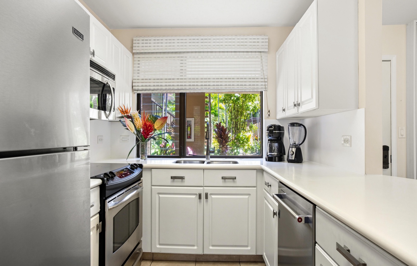 Step into your bright, beautifully organized kitchen, where sleek white cabinetry meets modern stainless appliances. Natural light filters through the window, framing vibrant greenery outside—making every meal feel fresh and inspiring.