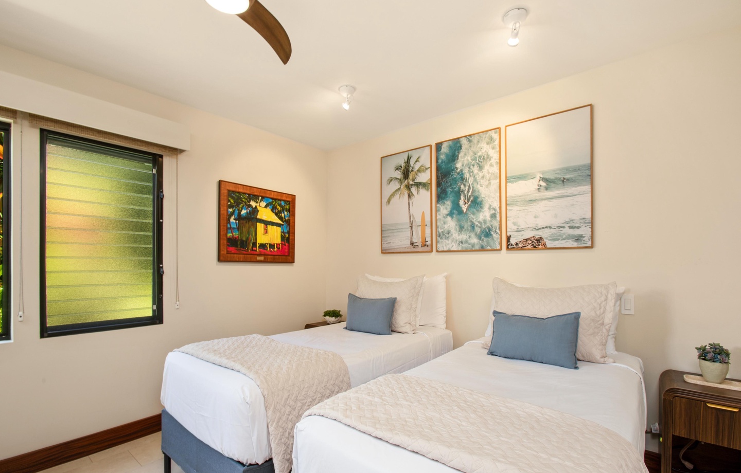Relax in this serene bedroom featuring twin beds dressed in crisp white linens and coastal art. The ceiling fan and soft blue accents create a peaceful, breezy retreat.