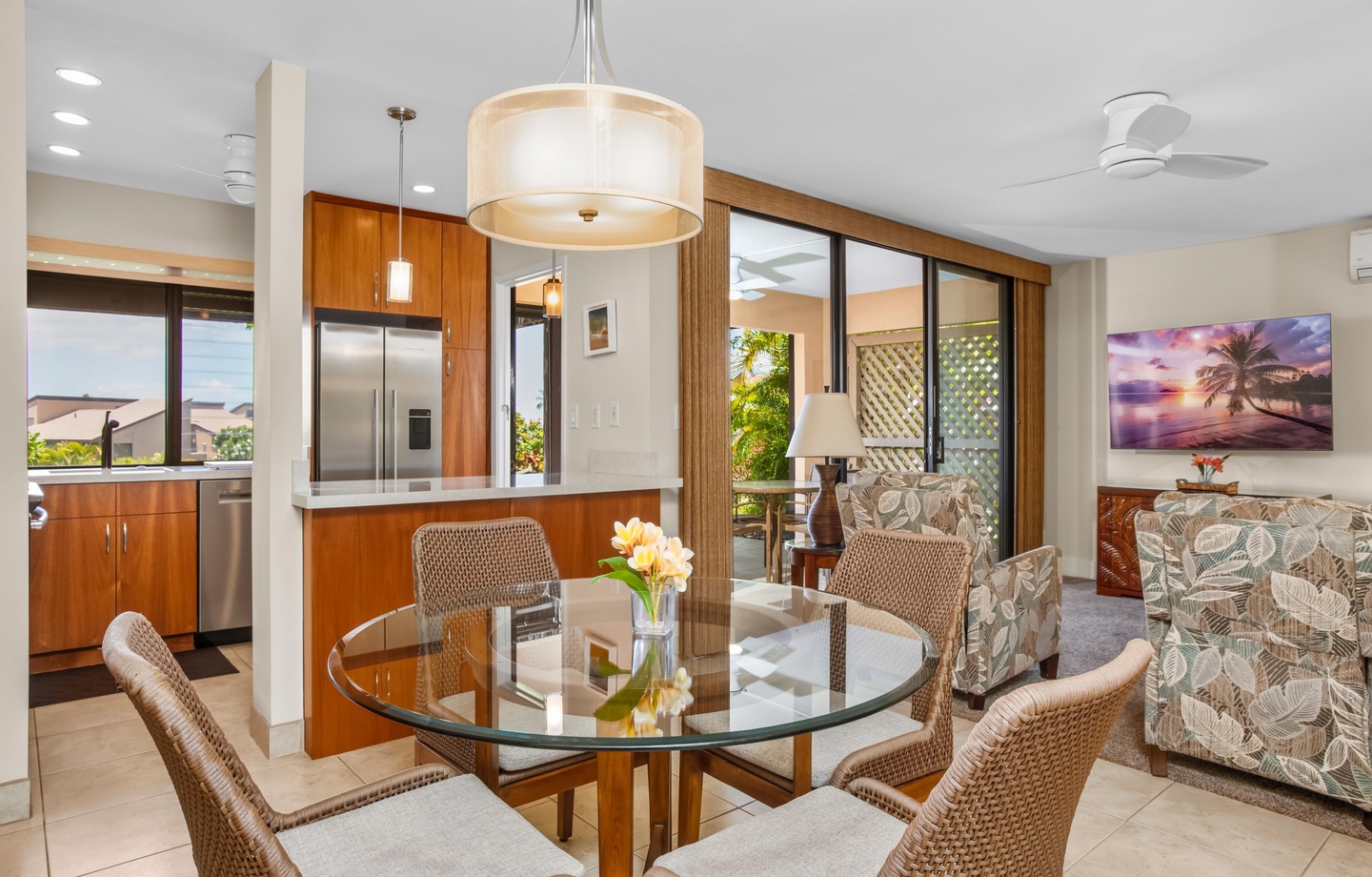 Gather around the elegant glass dining table where warm island breezes drift in from the lanai. Natural light fills this open-concept space, connecting your dining moments to tropical greenery just beyond the sliding doors.