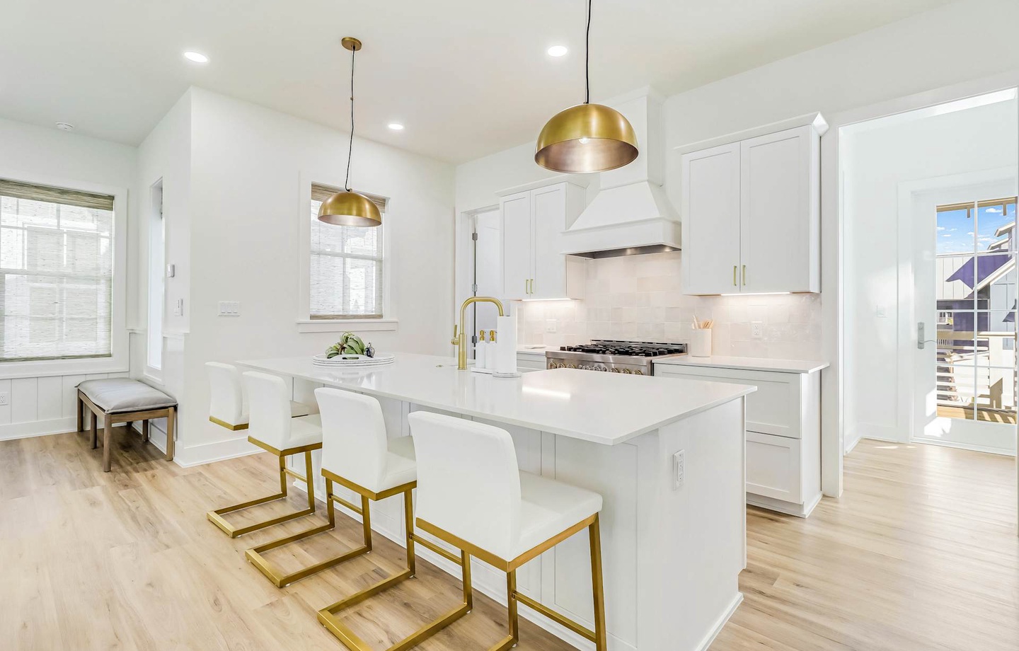 Bright, modern kitchen featuring elegant gold pendant lights, sleek white cabinetry, and a spacious island perfect for gathering. Large windows flood the space with natural light.