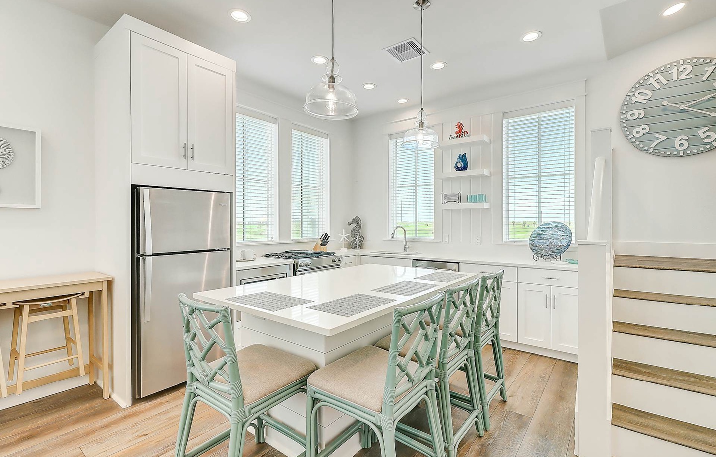 Your bright coastal kitchen awaits with stainless appliances, a large island for meal prep, and charming mint-green chairs that invite you to linger over breakfast with a view.