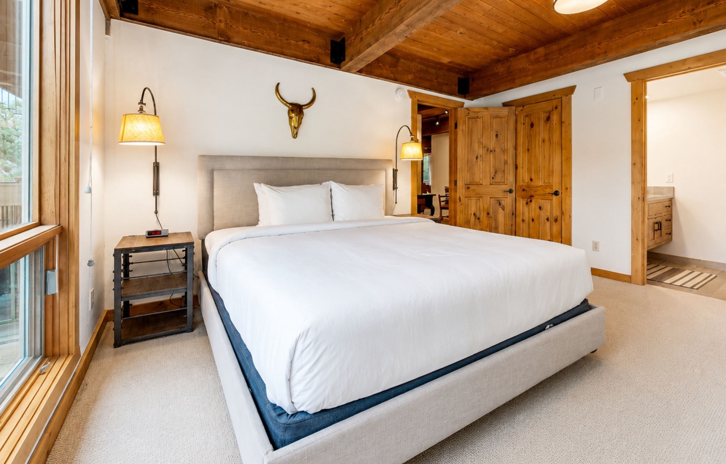 Sink into plush bedding under warm wood beams in your rustic-chic bedroom. Clean lines meet mountain charm with custom lighting, cozy textures, and peaceful white walls framing your alpine escape.