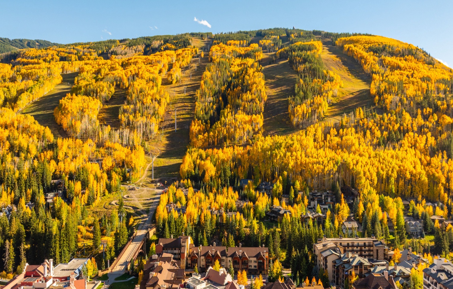 A stunning mountain resort blanketed in golden autumn foliage, with ski runs cutting through vibrant aspen groves and charming alpine village buildings nestled at the base.