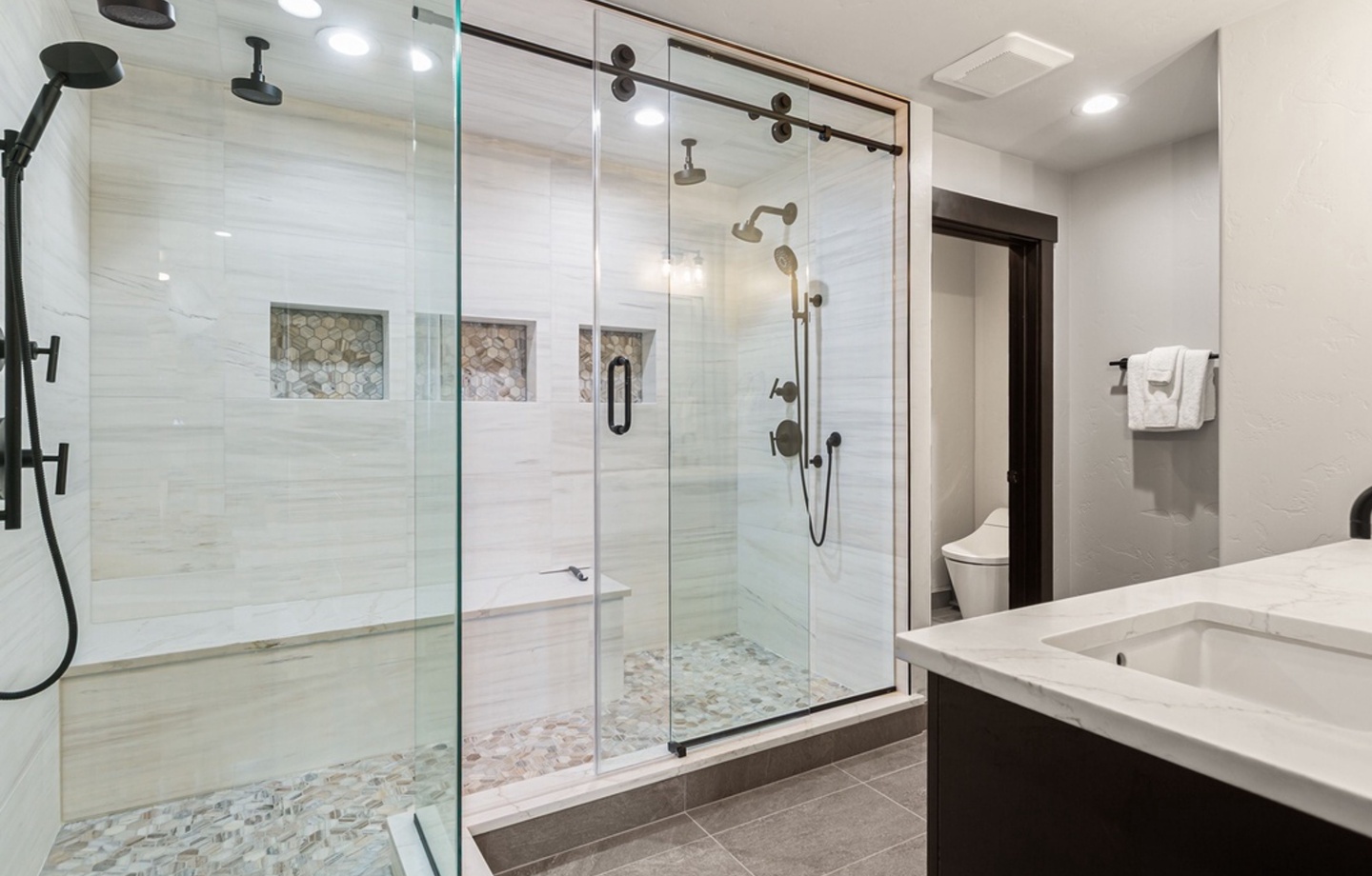 Step into your luxurious spa-style bathroom with a spacious walk-in shower featuring dual rainfall and handheld showerheads, elegant mosaic tile flooring, and modern fixtures throughout.