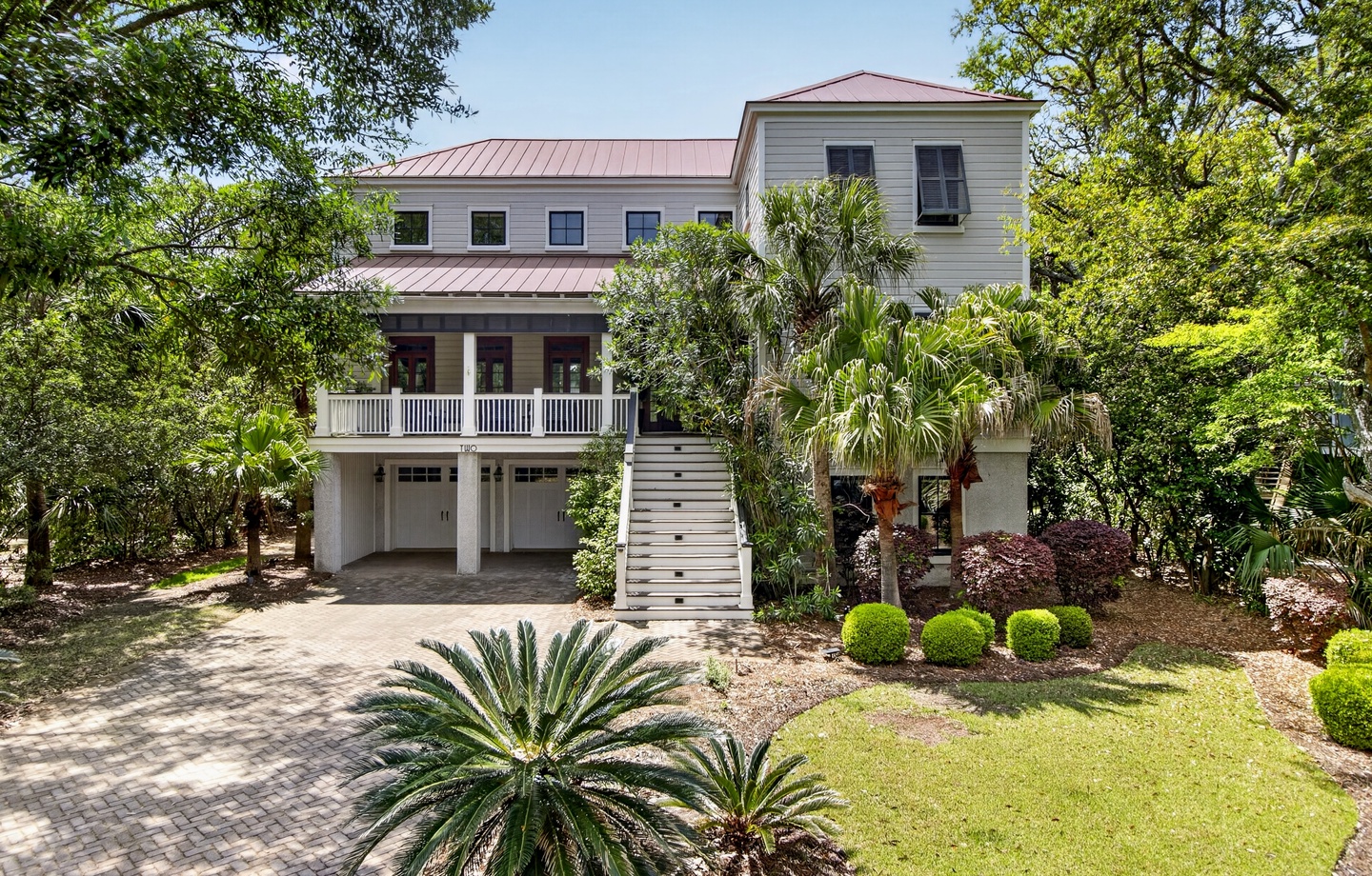 Elegant coastal home with mature tropical landscaping and covered parking nestled among towering trees.