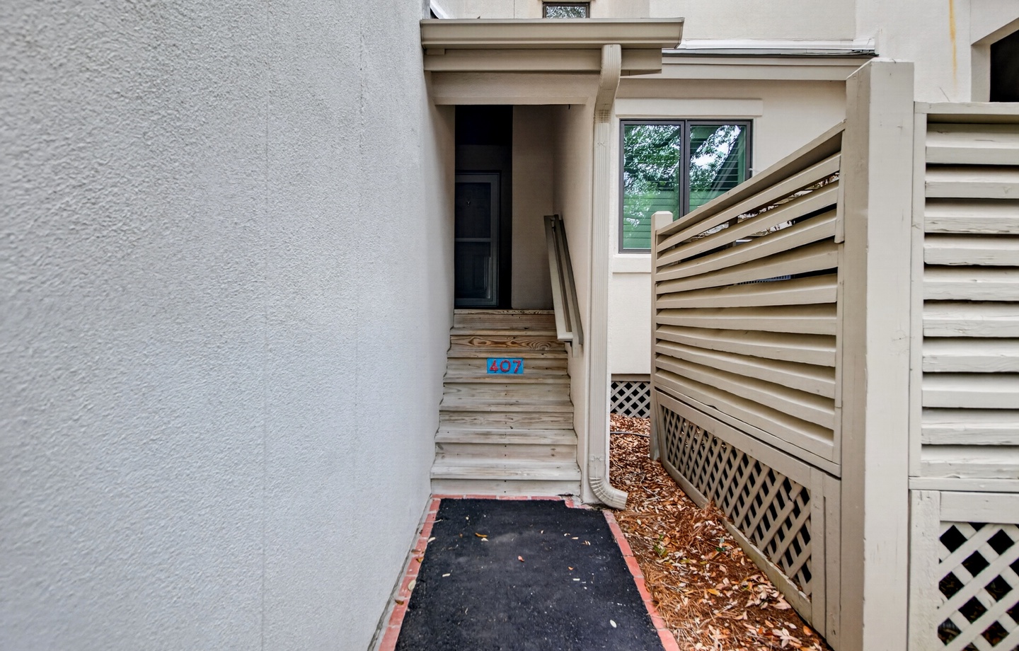 The property entrance is accessed via wooden stairs leading to the front door, marked with unit number 407, surrounded by clean stucco exterior and privacy fencing.