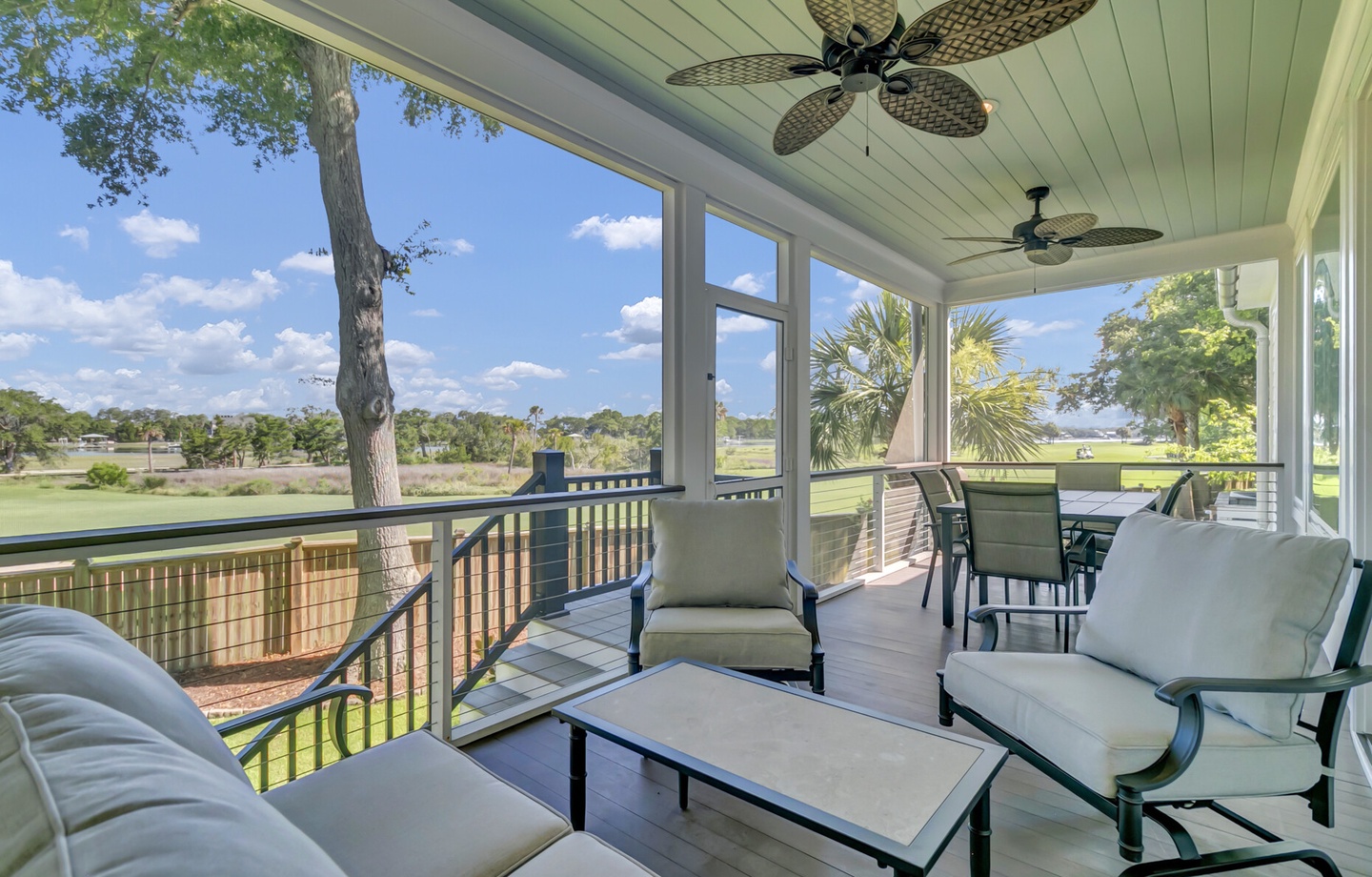 A screened porch with comfortable seating overlooks a golf course and natural landscape, offering a peaceful spot to relax and enjoy the view.