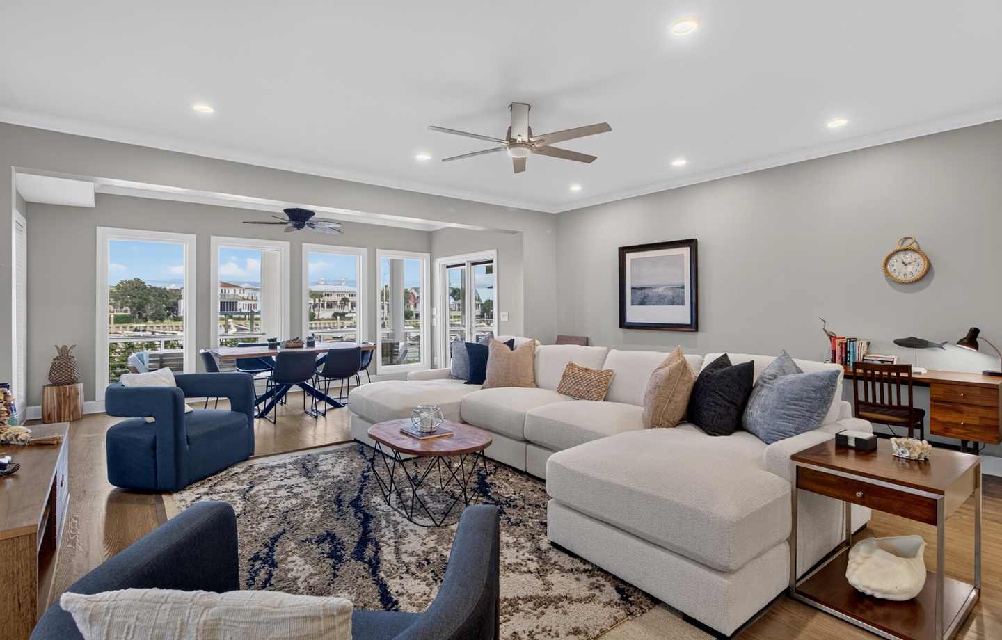 Bright living space with expansive windows flooded with natural light, ceiling fan, and spacious sectional. Relax with stunning marina views from this waterside retreat.