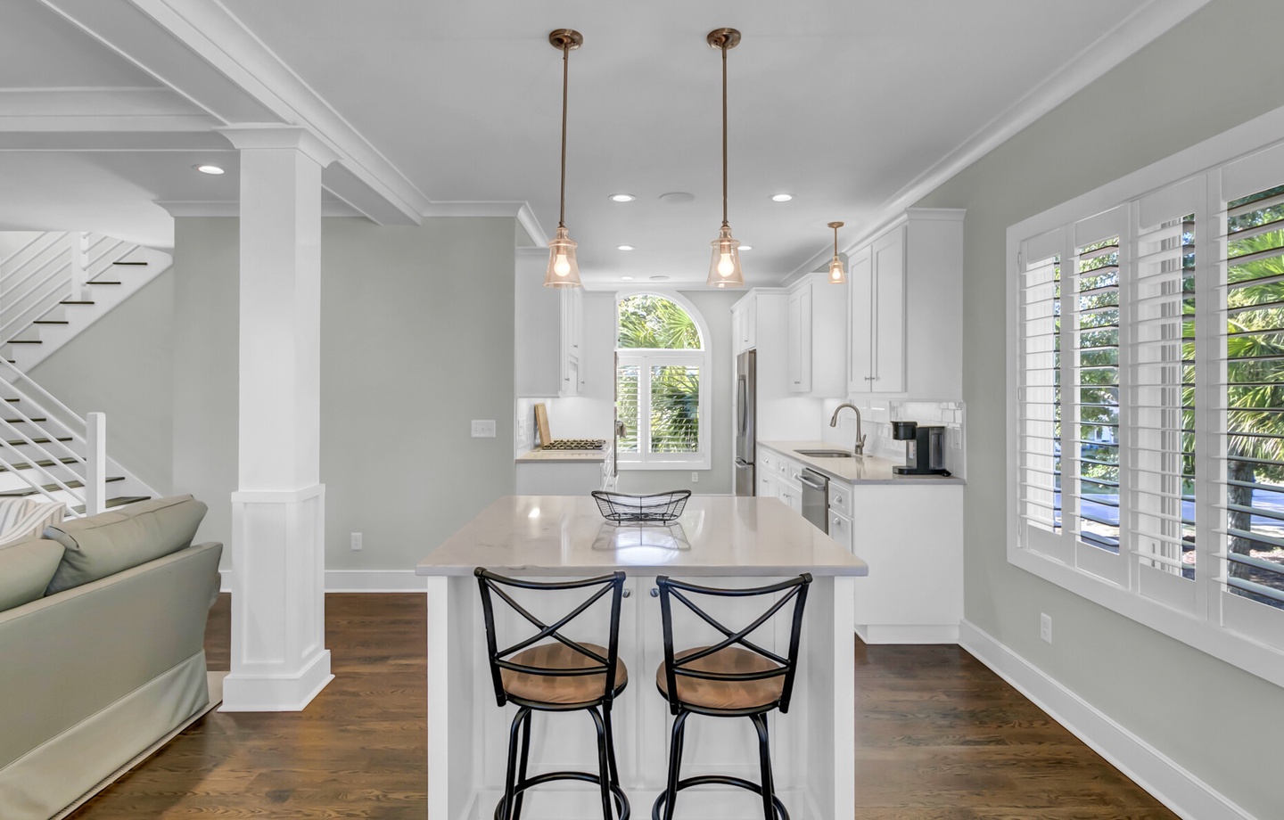 Gather at your sunlit kitchen island where coastal charm meets modern comfort. White cabinetry and gleaming countertops make meal prep a breeze while natural light streams through plantation shutters.