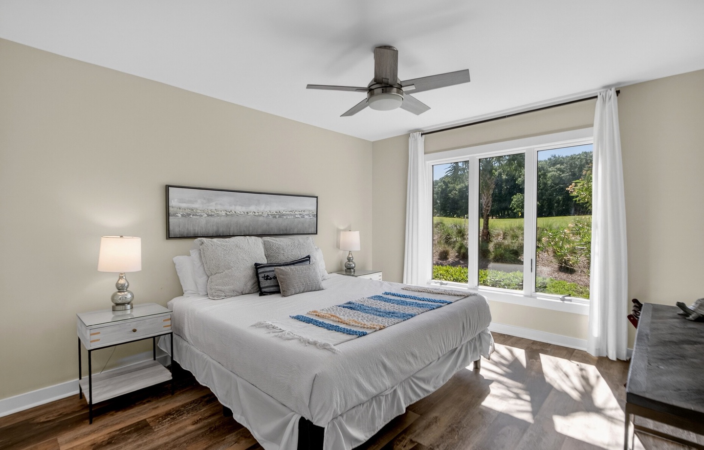Your serene bedroom features a plush bed, calming neutral tones, and bright natural light from large windows overlooking lush greenery.