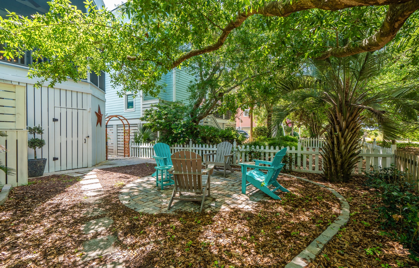 Your private backyard oasis awaits, with colorful Adirondack chairs shaded by mature trees—perfect for morning coffee or an afternoon read.