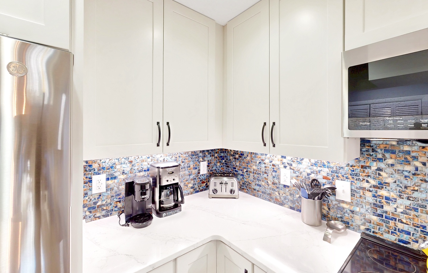 Your fully equipped kitchen features gleaming white cabinetry, a mosaic tile backsplash, and modern appliances ready for morning coffee or preparing meals during your stay.